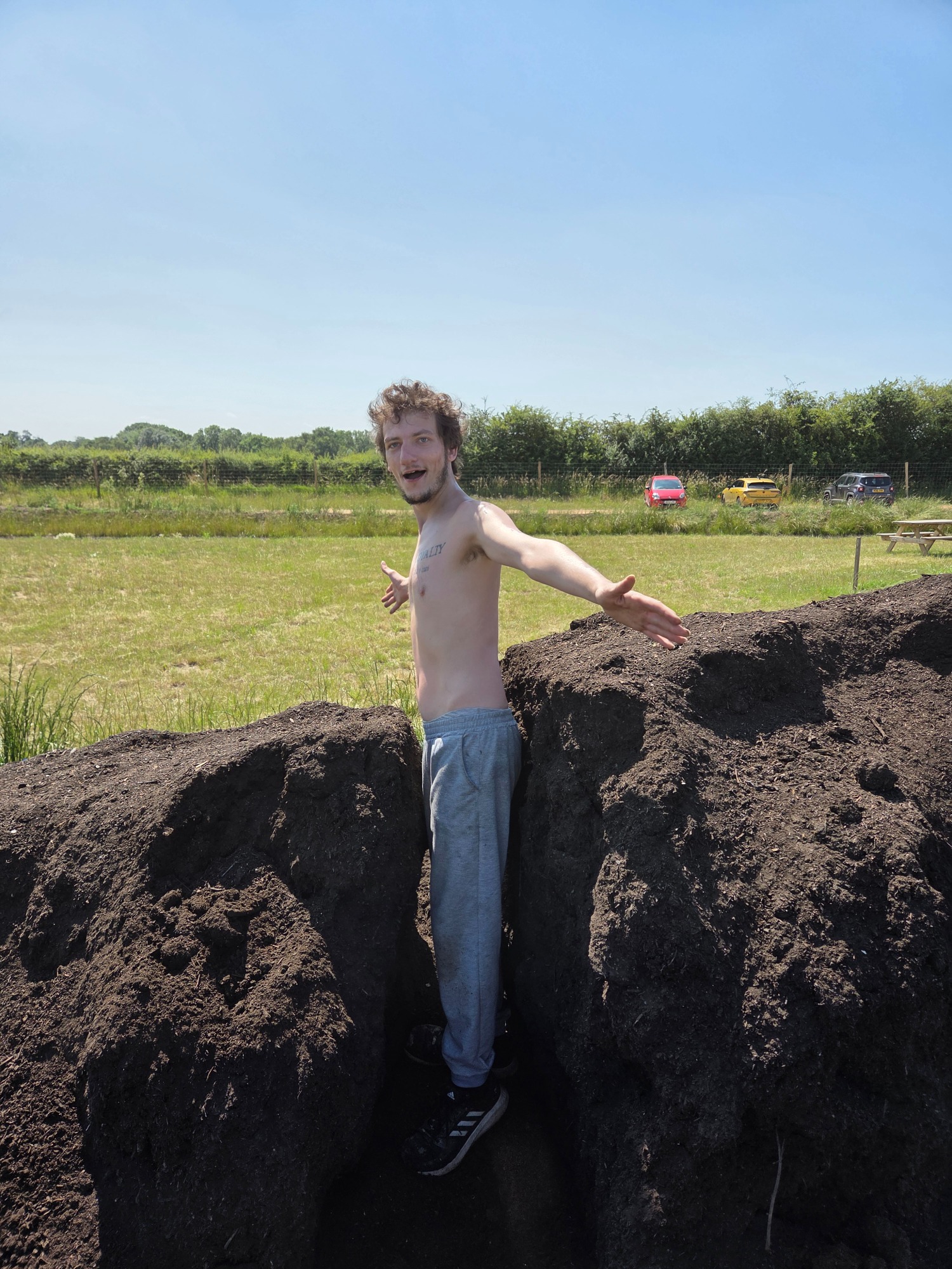 A shirtless young man standing between two large mounds of earth in a field.