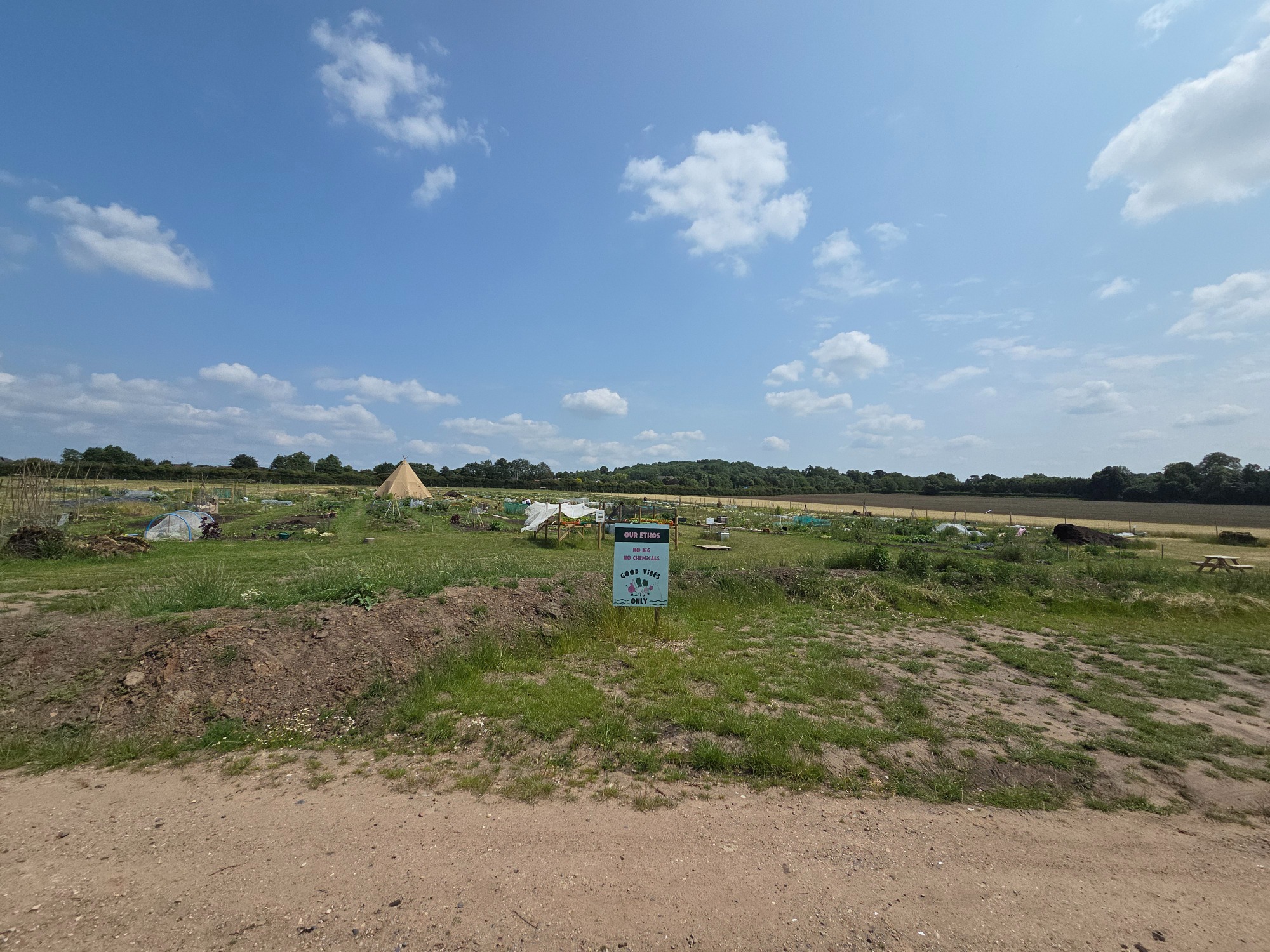 A rural landscape featuring fields, a dustbin, and a blue sky with scattered clouds.
