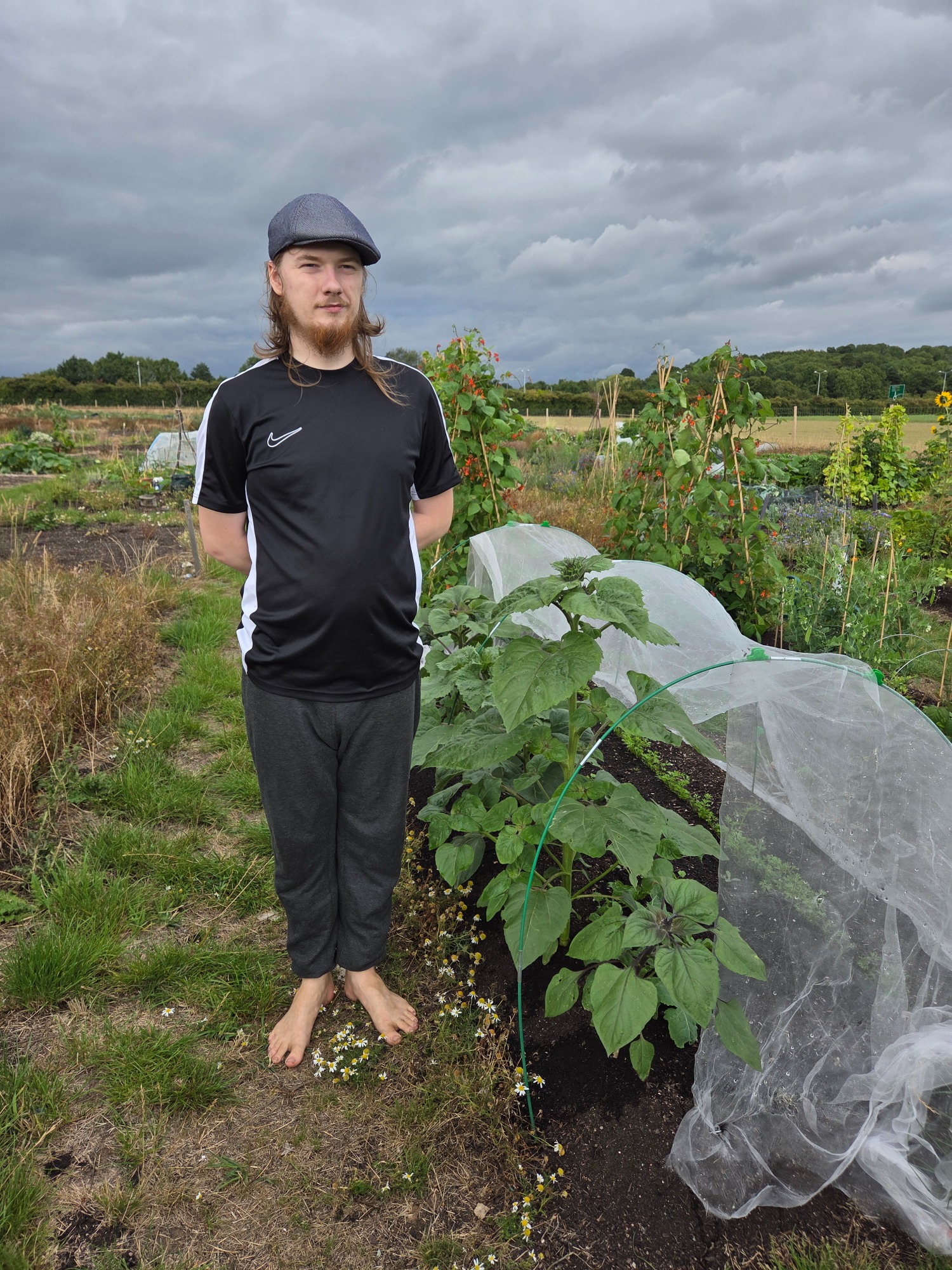 A person stands barefoot in a garden next to growing plants under a protective cover.