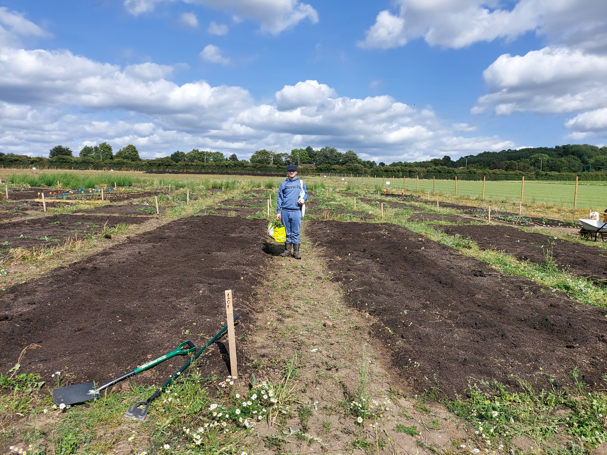 A person walking through a ploughed field on a sunny day, with tools nearby.