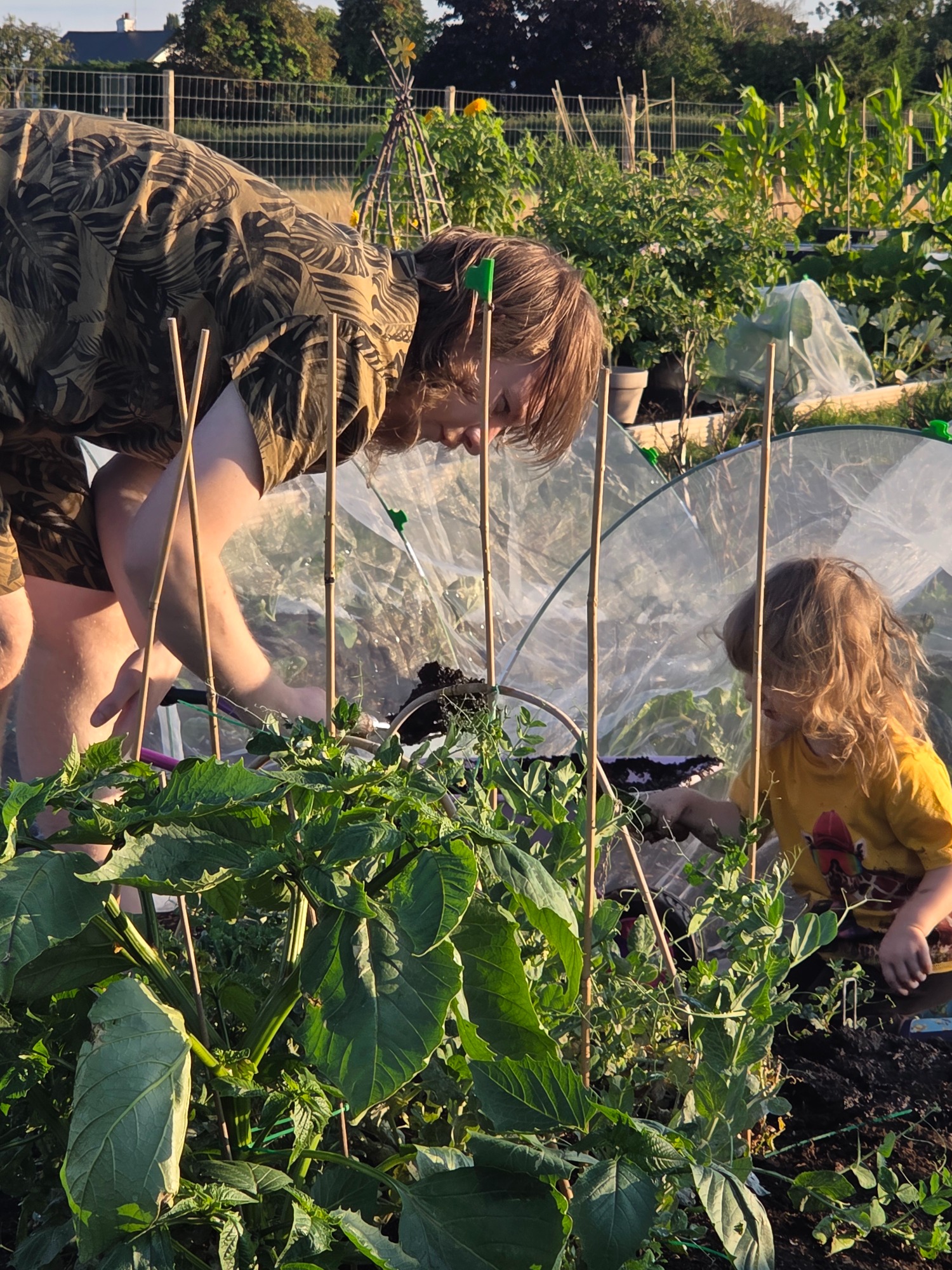 A woman and a child gardening, surrounded by plants and greenery.